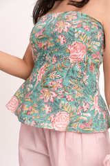A close-up of a woman wearing a strapless peplum top with a detailed floral print in teal green, pink, and yellow, paired with light pink pants.