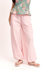 A person wearing light pink wide-leg pants with a floral print top, shown from the waist down against a plain white studio background.