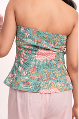 A woman shown from the back wearing a strapless floral top with a peplum hem. The top features a teal green background with a pink, red, and yellow floral pattern.