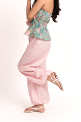 A woman modeling a strapless peplum top with a green tropical floral print and matching pink wide-leg pants, paired with white strappy flat sandals, against a plain white studio background.