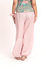 A person shown from the back wearing light pink wide-leg pants, a floral green top, and flat sandals against a plain light background.