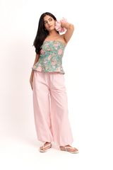 A woman modeling a strapless floral top with pink wide-leg pants and sandals, standing against a plain white studio background.