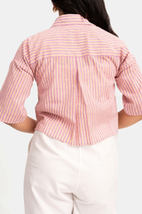 A person shown from the back wearing a pink striped short-sleeve button-up shirt and white pants against a plain white background.