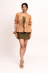 A woman modeling a short-sleeve floral cardigan with a tie-front detail over an olive green top, paired with an olive green mini skirt and beige platform sandals, against a plain white studio background.
