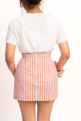 A woman shown from the back wearing a white short-sleeve t-shirt and a high-waisted, pink and white vertically striped mini skirt, set against a plain white background.