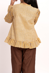 A woman shown from the back wearing a yellow and blue vertically striped blouse with a ruffled hem and brown pants, against a plain light background.