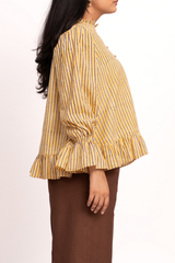 A woman shown from the side wearing a yellow and blue vertically striped blouse with a ruffled hem and brown skirt against a plain white background.