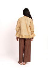A woman viewed from behind wearing a yellow and white vertically striped long-sleeve blouse with ruffled cuffs and hem, paired with brown wide-leg pants, against a plain white studio background.