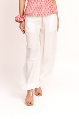 White wide-leg cropped pants with front patch pockets, shown on a model wearing a pink patterned top and clear-strap sandals against a light beige studio background.