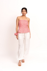 A woman modeling a pink and white patterned strapless tube top paired with white wide-leg pants and clear high-heeled sandals, standing against a plain white studio background.